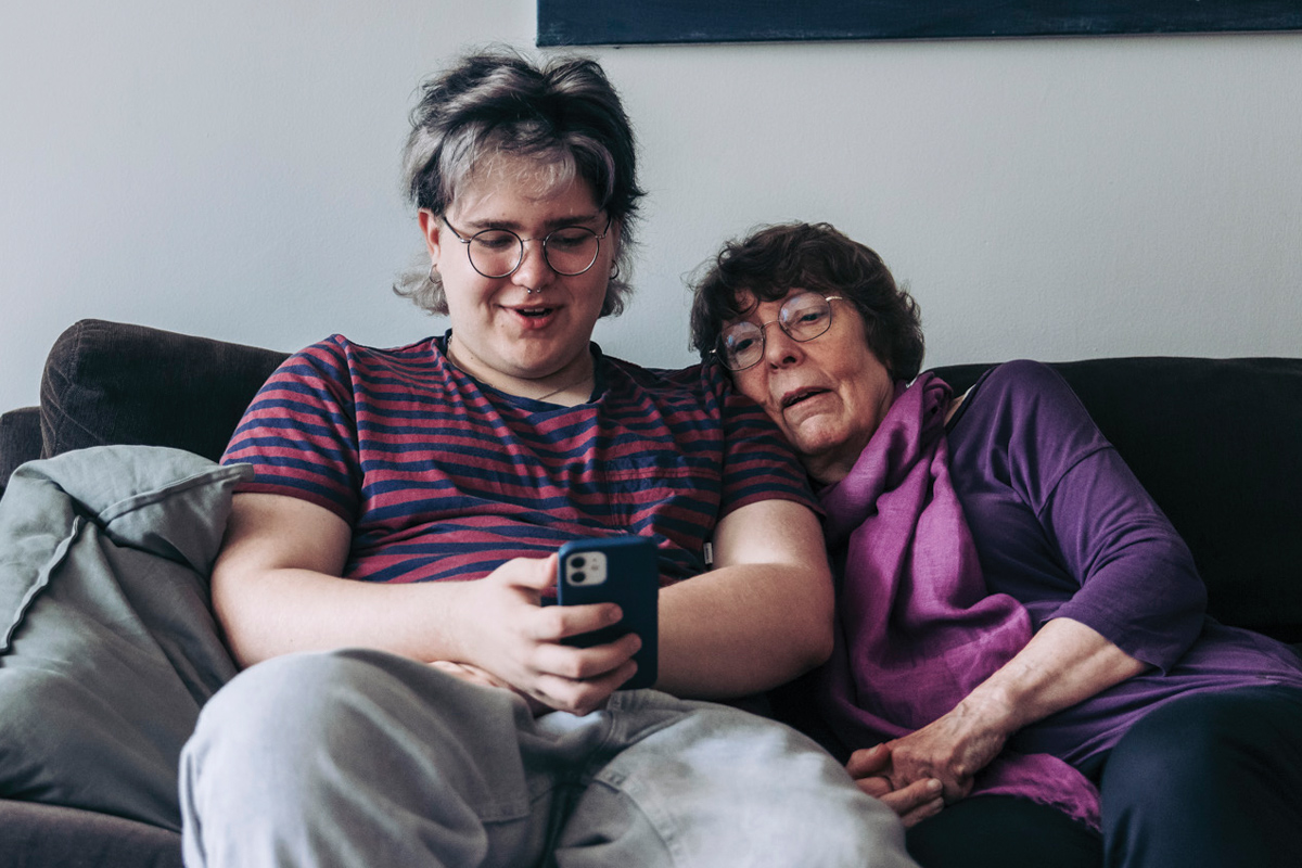 Teenage boy and elderly woman together on a sofa looking at a cellphone screen