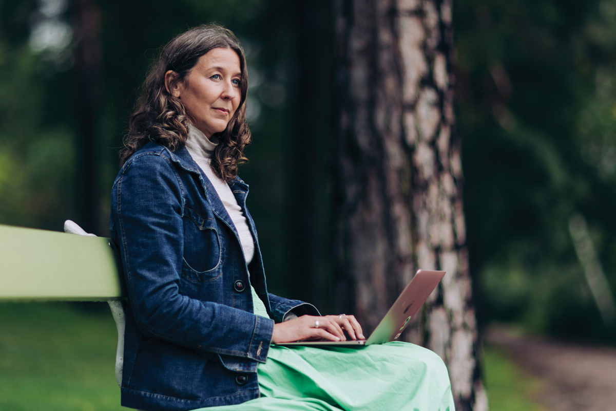 Woman on a bench outside with a laptop on her lap